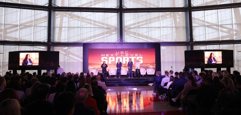 A stage that says "USC NEXT LEVEL SPORTS" on which four people are presenting.