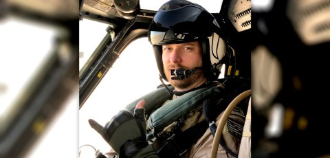 Male navy pilot in helicopter cockpit wearing helmet and flight suit