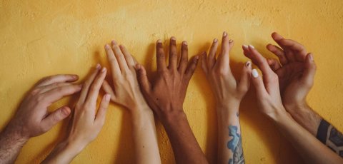 Hands reaching up on a yellow wall.