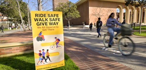 Yellow and white sign reads "Ride safe, walk safe, give way) as bicyclists and pedestrian walking pass each other
