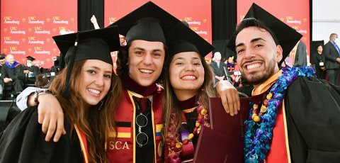 two male and two female students wearing graduation garb smile at the USC Annenberg 2023 commencement celebration.