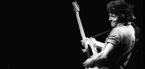 Bruce Springsteen playing guitar in black and white.