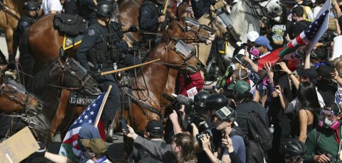 Police on horses with batons out stand amidst smartphone-wielding protesters. 