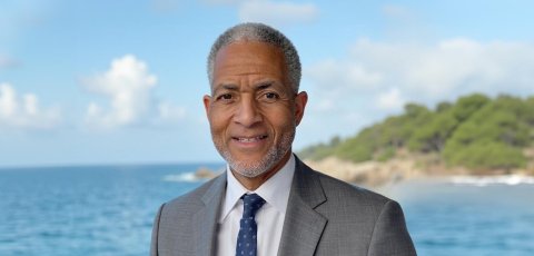 Andre Lapeyrolerie, from the shoulders up, smiling at the camera while wearing a suit and standing in front of an ocean with an island in the background. 