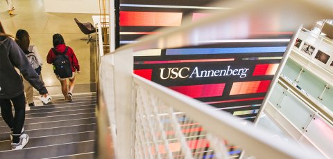 Students walking down a staircase while the Wallis Annenberg Hall Media Wall shines in the backgroud.