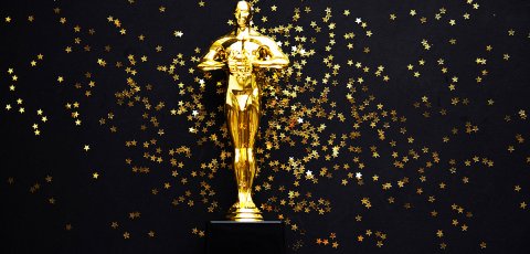 oscar award in front of black backdrop with gold confetti falling