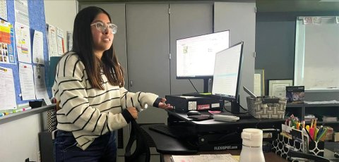 Wendy Chavez at the teacher's desk in a classroom.