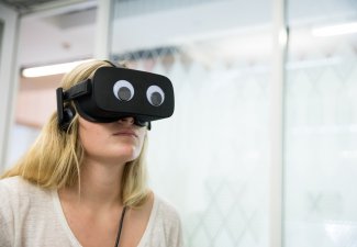 Photo of a person using a VR headset with googly eyes attached to it