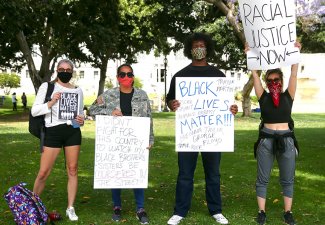 Photo of four people holding signs for Black Lives Matter and racial justice