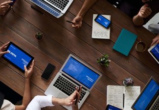 Photo of people working at a table with devices. 