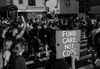 Photo of a protest with a visible sign that reads "fund care not cops"