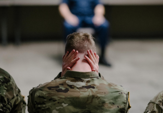 Photo of a military member with their hands on the back of their neck, sitting next to other members