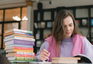 Photo of a person reading a book next to a stack of books
