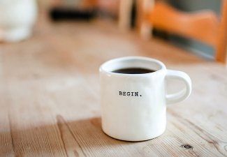 Photo of a coffee mug on table that reads "begin"