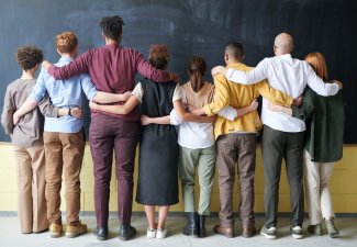 Group of people standing in doors in front of a chalk board with their arms around eachother