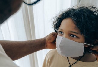 Photo of an adult putting a face mask on a child