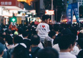 Photo of a crowd at the Hong Kong Protest and a kid on someone's shoulders wearing a shirt that said "I <3 my mom"