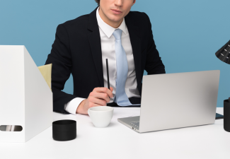 Photo of a person writing at a desk in front of a laptop computer