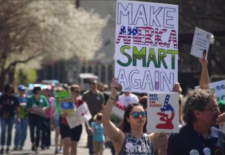 Photo of protesters with one holding a sign that says "Make America Smart Again"