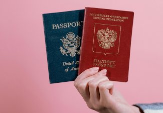 Someone holding two different passports against a pink background