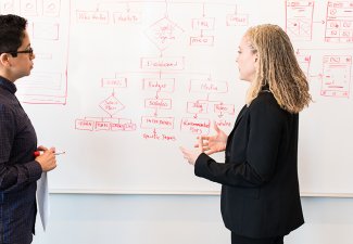 Photo of two people standing in front of a white board with illustrations on it