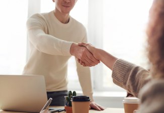 Two people shaking hands over a desk. 
