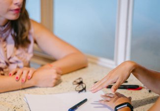 Photo of two people sitting across eachother with papers on the table, conversating