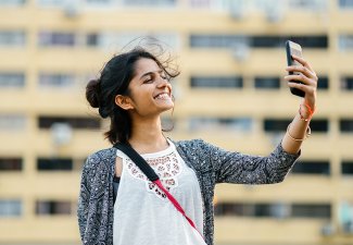 Photo of a person holding their phone and smiling at it