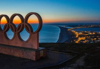 Olympic ring statue over city at sunset. 