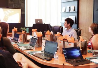 Photo of people sitting around a table with computers and bags