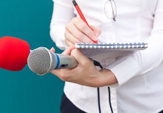 Photo of a person writing on a writing pad holding two different microphones