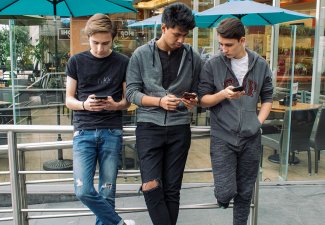 Photo of three teens standing looking at their phones