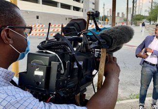 Photo of a person recording another person with a media camera on the street