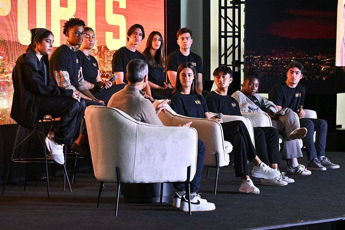 Students sit in elevated chairs on a stage with Jimmy Pitaro. 