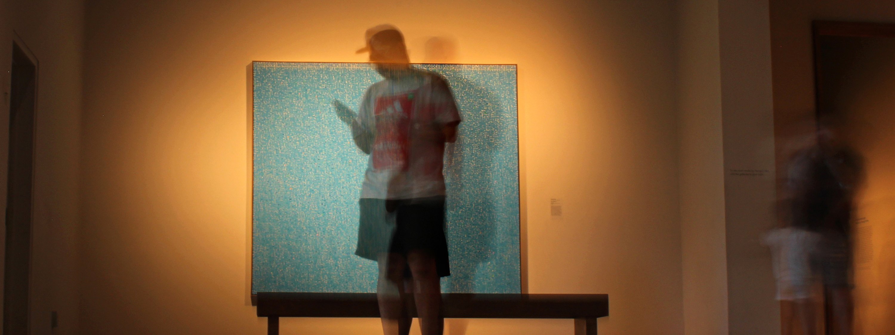 Blurred person standing in front of an art piece on their phone.