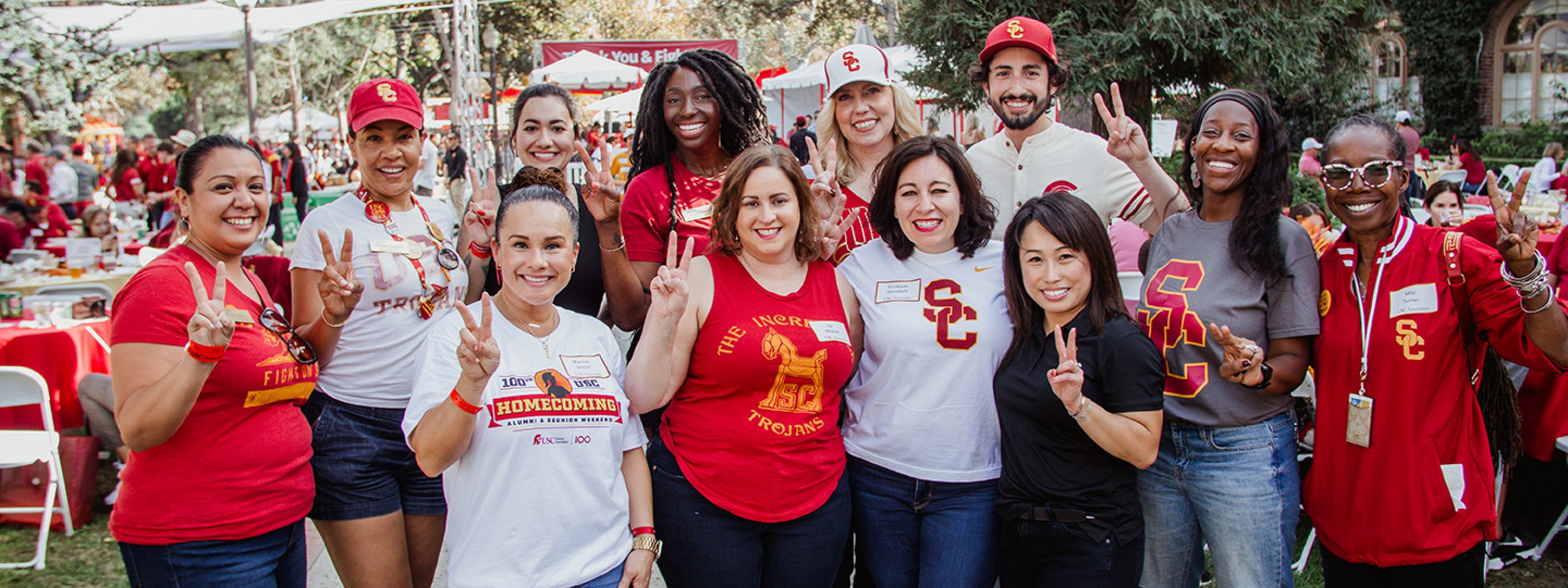A group of USC alumni holding up the "Fight On!" sign on campus