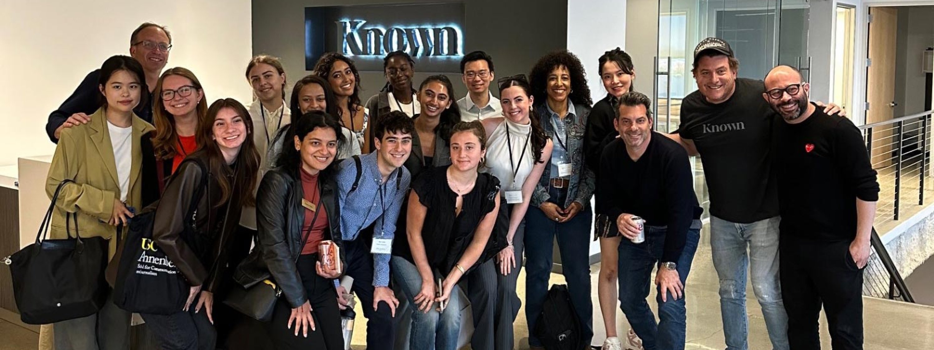 A group of students and faculty smile for a photo in front of a logo that says "Known."