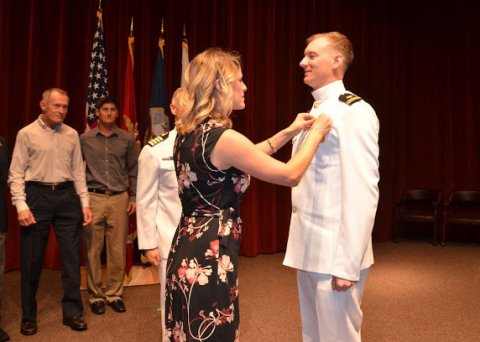 Man in white U.S. Navy dress uniform smiles while being pinned by woman