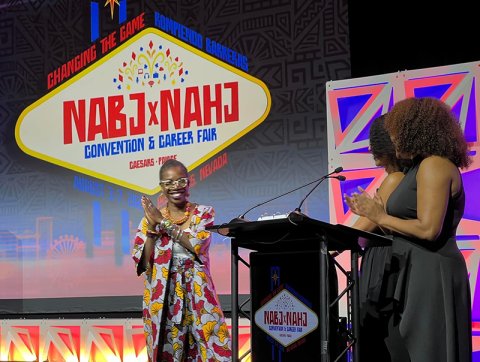 Miki Turner receives the NABJ Educator of the Year award on stage next to two presenters.