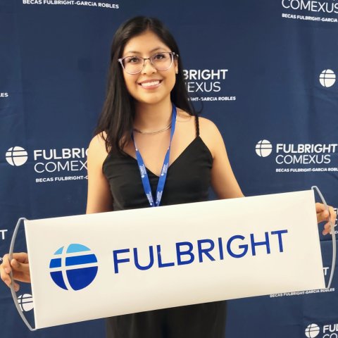 USC Annenberg Public relations student and Fulbright scholar Dany Rodríguez Martínez holds a white "Fulbright" sign in front of a blue wall.