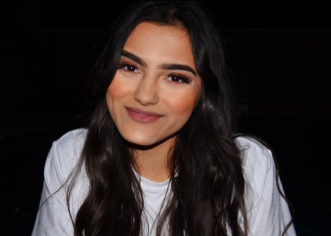 young hispanic woman in white shirt in front of black background smiles for camera