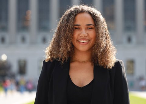 young black woman in black sweater smiles in front of national building