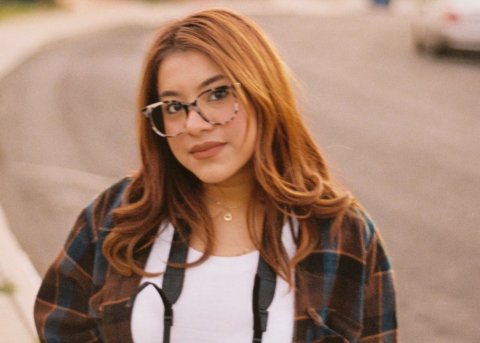 Young hispanic women poses on street with camera strap around her neck