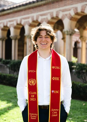 male college graduate smiles for camera wearing red and gold stole