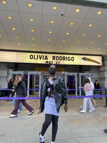 black female college student stands in front of theatre marquee that says Olivia Rodgrigo May 27