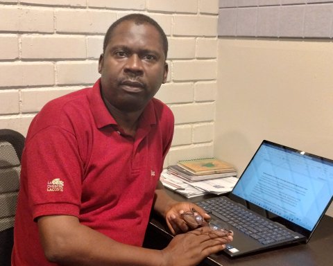 Nigerian man sits in front of laptop and works on graduate student project