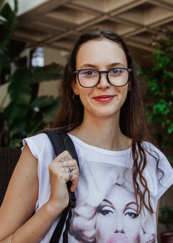 Italian college woman wearing glasses smiles for camera and poses with backpack