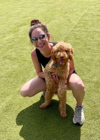 women in early 20s wearing sunglasses poses with labradoodle puppy. 