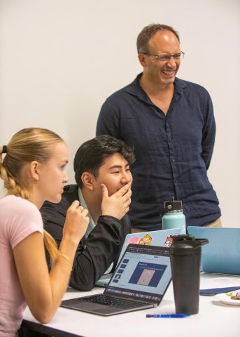 Professor stands and laughs with two seated students during class