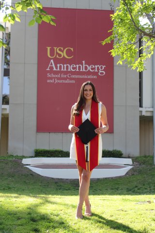 female college graduate stands in front of USC Annenberg mural 